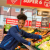 A young Black woman in an ALDI uniform smiles as she reaches over a fruit and veg section in an ALDI store.