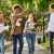 Four young apprentices carrying books through a very green outdoor space high-five and laugh together