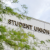 Image of a large concrete building with the words STUDENT UNION in large signage. The sign is partially obscured by a nice green tree.