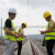Three people who could be rail apprentices on the RailBEE apprenticeship scheme in yellow vests and hard hats standing on railroad tracks